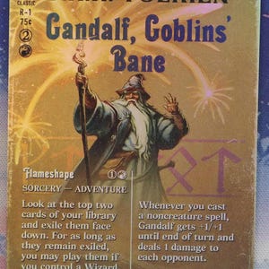 Peut inclure: Une carte à collectionner rectangulaire illustrant un magicien à longue barbe blanche tenant un bâton, entouré de feux d'artifice. Le texte indique J.R.R. TOLKIEN, Gandalf, Goblins' Bane, Flameshape, ainsi que des règles et statistiques.