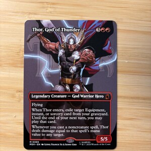 May include: A collectible trading card titled Thor, God of Thunder featuring a comic book illustration of the character with a winged helmet, red cape, and hammer. The card text includes abilities, a 5/5 power and toughness, and Marvel branding.