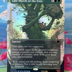 Könnte beinhalten: Eine Magic: The Gathering Sammelkarte mit dem Titel Last March of the Ents, die eine große, grüne, baumartige Kreatur zeigt, die zwei kleine Figuren in ihren Ästen trägt. Der Kartentext enthält die Zauberdetails und ein Zitat von Baumbart.