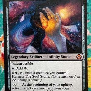 May include: A Magic: The Gathering card titled "The Soul Stone." The card features an illustration of hands holding a glowing orb against a cosmic background. Text details the card's abilities.