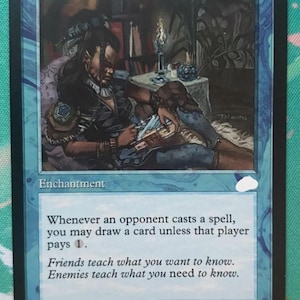 May include: A blue Magic: The Gathering trading card titled Rhystic Study. The card features an illustration of a figure reading by candlelight, with the text: Whenever an opponent casts a spell, you may draw a card unless that player pays 1.