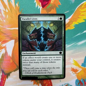 Peut inclure: Une carte à collectionner Magic: The Gathering intitulée Parallel Lives, présentant une carte enchantement avec une bordure noire, un cadre vert et une illustration de deux têtes de loup émergeant d'un fond sombre avec des yeux jaunes.