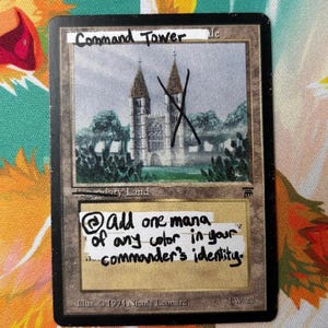 May include: A rectangular trading card featuring a central illustration of a stone cathedral with two towers. White tape strips are applied over the card with the handwritten text Command Tower and Add one mana of any color in your commander's identity.