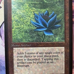 Könnte beinhalten: Eine rechteckige Sammelkarte mit dem Titel Black Lotus und den Kosten 0. Die Karte zeigt eine blaue Lotusblüten-Illustration auf grünem Hintergrund, den Text Mono Artifact und den Regeltext: Adds 3 mana of any single color of your choice to your mana pool, then is discarded. Tapping this artifact can be played as an interrupt. Illus. Christopher Rush.