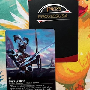 May include: A rectangular trading card featuring the Esper Sentinel character in silver armor against a blue sky, with text reading Esper Sentinel, Artifact Creature - Human Soldier, and game rules. Behind it is a black card with the text PROXY PROXIESUSA.