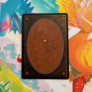 May include: A rectangular trading card with a brown back and a black border. The back of the card features a brown oval with coloured dots. The card is set against a colourful background with illustrations of birds.