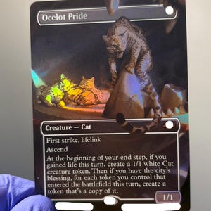 Op de afbeelding: Een rechthoekige ruilkaart getiteld Ocelot Pride met een holografische afwerking. De afbeelding toont een gevlekte kat op een rots boven kleinere katten. De tekst bevat Creature - Cat, First strike, lifelink, Ascend en spelregels.