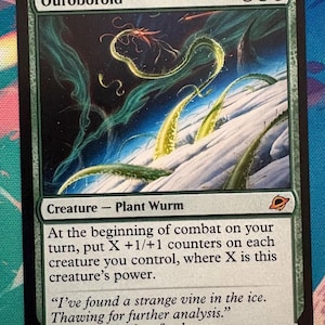 May include: A Magic: The Gathering card titled "Ouroboroid." The card features an illustration of a plant wurm in a blue and green icy environment. The card text describes the creature's abilities and includes a quote from the Meltstrider log.