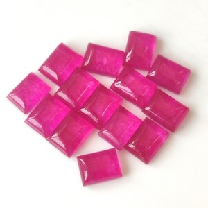 May include: A collection of fourteen rectangular, faceted gemstones in a vibrant, translucent magenta pink color. Each stone features a smooth, polished surface with beveled edges, arranged in a loose cluster against a plain white background.