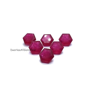 Op de afbeelding: Zes gefacetteerde, zeshoekige edelstenen in een levendige magenta tint op een witte achtergrond. De edelstenen hebben een gepolijst, reflecterend oppervlak dat het licht vangt. De compositie is helder en toont de kleur en vorm van de stenen.