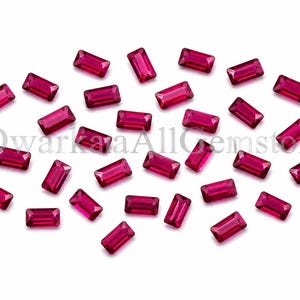 Peut inclure: Plusieurs pierres précieuses rectangulaires rouge foncé sont dispersées sur un fond blanc. Les gemmes, polies et réfléchissantes, présentent des coupes précises. L'image évoque le luxe et l'élégance.
