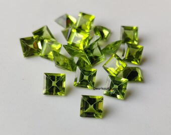 May include: A collection of faceted, square-cut peridot gemstones in various shapes and sizes. The gemstones are a vibrant, translucent green color, with a polished, reflective surface. The gems are scattered on a white surface.