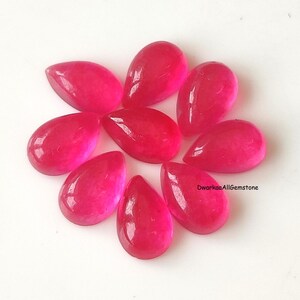 May include: A collection of eight vibrant, hot pink gemstones, each cut into a smooth, polished teardrop shape. The stones are arranged in a circular pattern, displaying a translucent quality and a glossy finish. The text DwarkaaAllGemstone is visible.