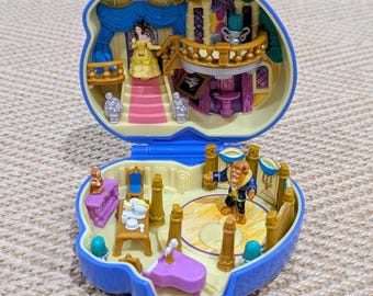 May include: A blue plastic clamshell-shaped playset that opens to reveal a two-level interior. The top level features a staircase and balcony, while the bottom level includes a ballroom floor, a small piano, a table with tea service, and two figures.