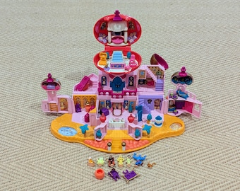 May include: A pink and gold miniature playset resembling a palace, with multiple rooms, a slide, and small figurines. The playset is open, revealing interior details and accessories. A fun toy for imaginative play.