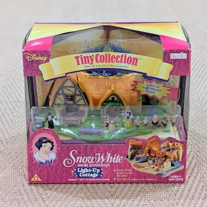 May include: A Disney Tiny Collection Snow White and the Seven Dwarfs Light-Up Cottage playset. The box is pink and yellow, with the Disney and Bluebird logos. The set includes miniature figures and a cottage, with the text 'Lights up in 3 different places!'