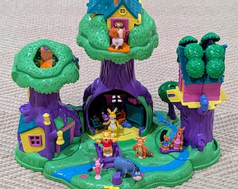 May include: A colorful Winnie the Pooh playset featuring a treehouse design with multiple levels and figures of Pooh, Piglet, Tigger, Eeyore, and Rabbit. The playset has a green base with a blue river and a yellow sign.