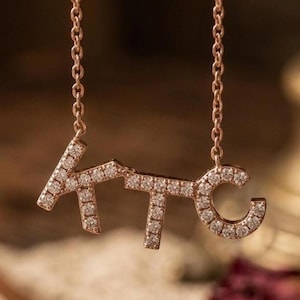 May include: A rose gold necklace spelling out the letters "KTC". The letters are embellished with small diamonds. The necklace hangs from a fine chain, creating an elegant and personalized accessory. The chain is approximately 40 cm long.