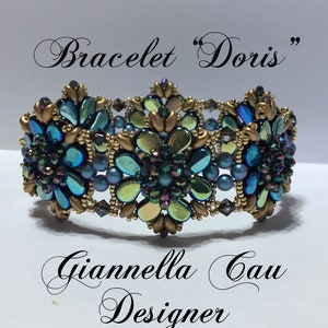 May include: A gold and teal beaded bracelet with a floral design. The bracelet is labeled "Bracelet "Doris" Giannella Gau Designer".