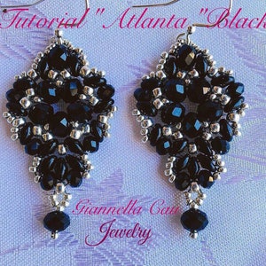 May include: A pair of black and silver beaded earrings with a teardrop shape. The earrings are made with small black beads and silver beads. The earrings are hanging from silver hooks. The earrings are labeled "Tutorial "Atlanta" Black" and "Giannella Cau Jewelry".