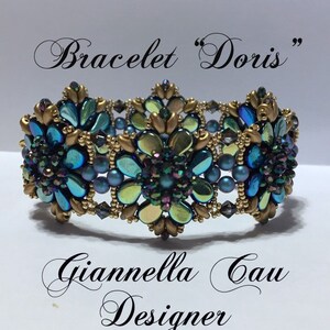 May include: A gold and blue beaded bracelet with a floral design. The bracelet is labeled "Bracelet "Doris" Giannella Gau Designer".