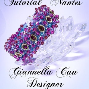 Peut inclure: Un bracelet en perles de couleur violette et bleue avec des accents dorés. Le bracelet est posé sur une surface en cristal transparent. Le texte "Tutorial "Nantes" Giannella Gau Designer" est visible sous le bracelet.