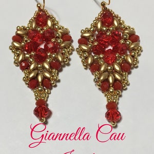 May include: A pair of red and gold beaded earrings with a diamond shape and a dangling red bead. The earrings are handmade and feature a delicate design. The earrings are labeled "Giannella Cau Jewelry".