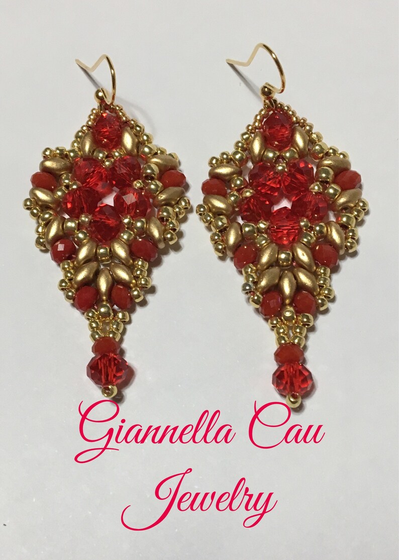 May include: A pair of red and gold beaded earrings with a diamond shape and a dangling red bead. The earrings are handmade and feature a delicate design. The earrings are labeled "Giannella Cau Jewelry".
