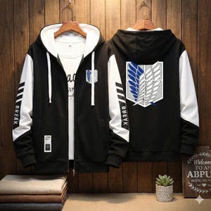 May include: Black zip-up hoodie with white sleeves and hood lining. Features a logo on the chest and back, with the word "BREAK" on the left sleeve. The hoodie is displayed on a wooden background.