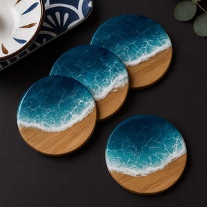 Peut inclure: Ensemble de quatre dessous de verre ronds avec un motif de plage. Les dessous de verre présentent une base en bois avec un dessus en résine bleue et blanche, imitant les vagues de l'océan. Diamètre d'environ 10 cm.