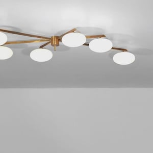 May include: A contemporary ceiling light fitting featuring a brass finish and several white, globe-shaped lights. The fitting has a starburst design, with the lights distributed along the arms. It is mounted on a white ceiling.