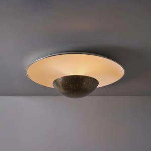 May include: A contemporary ceiling light. It features a large, circular, cream-coloured shade and a smaller, bowl-shaped, bronze-toned light fixture below. The bronze fixture has small, evenly spaced holes. The light is on, illuminating the room.