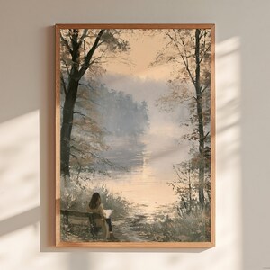 Könnte beinhalten: Ein gerahmter Wandkunstdruck, der eine ruhige Landschaft mit einer auf einer Bank am See sitzenden Person zeigt. Die Szene besticht durch hohe Bäume, sanftes goldenes Licht und eine neblige Atmosphäre in gedeckten Erdtönen, in einem Holzrahmen.