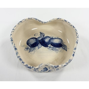 May include: Cream-colored ceramic bowl in a heart shape, featuring a hand-painted design of blue apples with leaves and flowers. The rim is decorated with a blue floral pattern. A charming piece for kitchen decor.