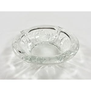 May include: A clear, round glass ashtray with a floral design etched into the sides. The ashtray has a shallow bowl shape and is made of thick, clear glass. The floral pattern is visible throughout the ashtray.