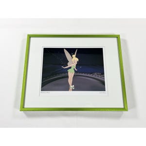 May include: A framed art print featuring a blonde fairy with translucent wings wearing a green dress and white slippers. The character stands on a dark circular surface against a dark background. The text reads "Precious Pixie" and "Not For Sale".