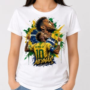 May include: A white t-shirt featuring a graphic print of soccer player Neymar Jr. The design includes a yellow jersey with the number 10, a portrait, and a Brazilian flag background with green, yellow, and blue paint splatters and the text OUSADIA ALEGRIA FE JR.