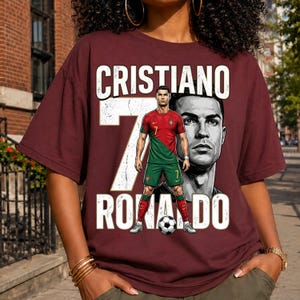 May include: A maroon short-sleeve t-shirt featuring a graphic of Cristiano Ronaldo in a red and green soccer uniform. The design includes the text CRISTIANO RONALDO, a large white number 7, a black and white portrait, and a soccer ball at the feet.