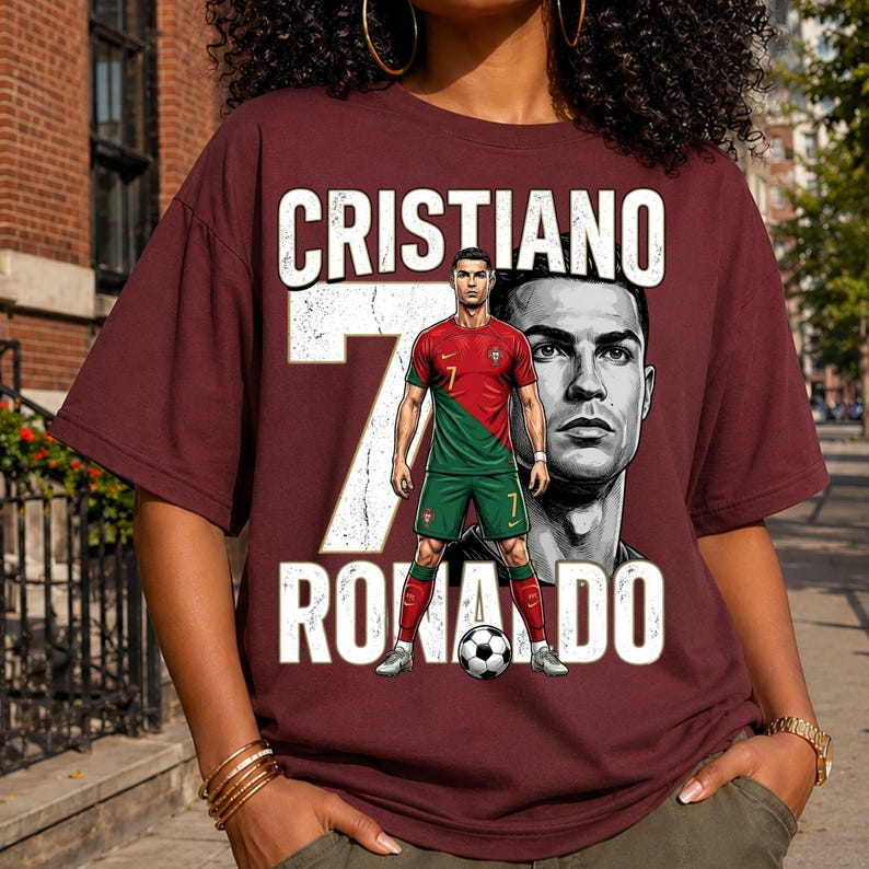 May include: A maroon short-sleeve t-shirt featuring a graphic of Cristiano Ronaldo in a red and green soccer uniform. The design includes the text CRISTIANO RONALDO, a large white number 7, a black and white portrait, and a soccer ball at the feet.
