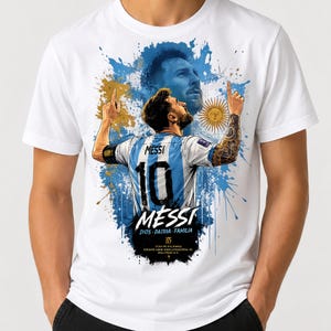 May include: White t-shirt featuring a graphic of a soccer player in a blue and white jersey with the number 10. The design includes the player's name, "MESSI," and a portrait, set against a blue and gold background.