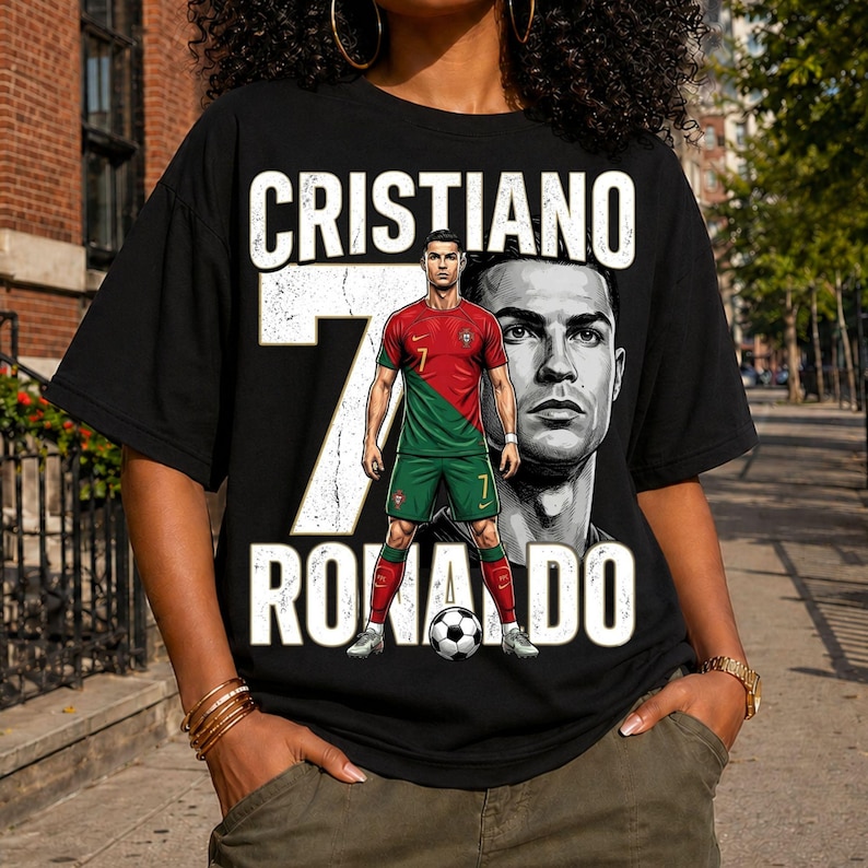 May include: A black t-shirt featuring a graphic print of Cristiano Ronaldo in a red and green soccer uniform. The design includes the text CRISTIANO RONALDO in large white letters, a large number 7, and a soccer ball at the bottom of the graphic.