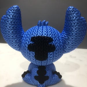 Op de afbeelding: Blauw beeldje van een stripfiguur met grote oren en een zwarte vlek op de borst. Het beeldje heeft een getextureerd, gebreid uiterlijk. Het personage zit.