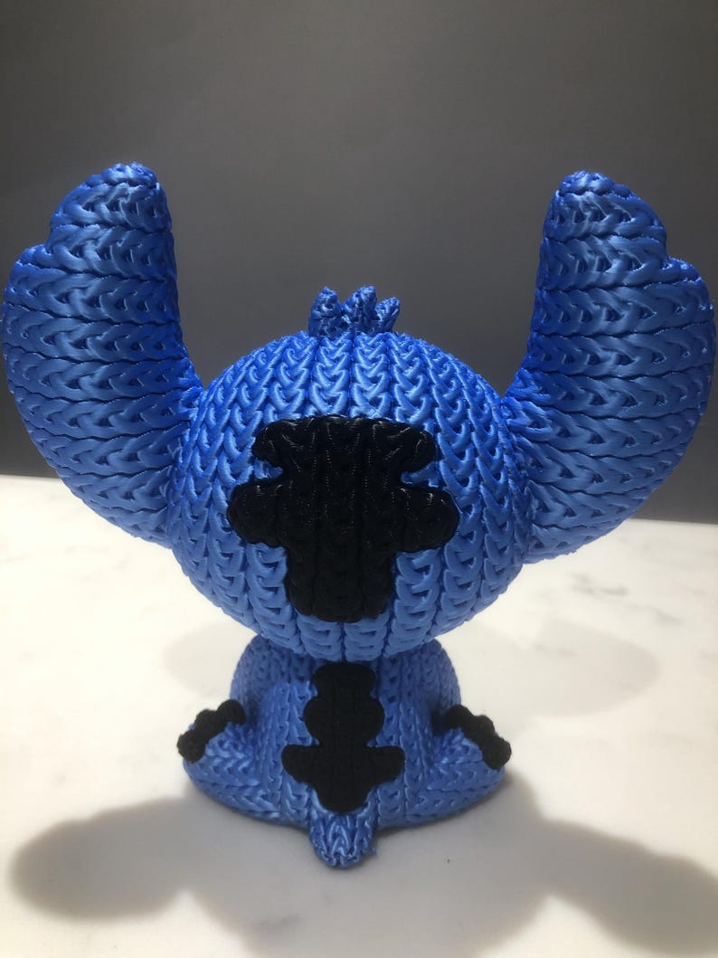 Op de afbeelding: Blauw beeldje van een stripfiguur met grote oren en een zwarte vlek op de borst. Het beeldje heeft een getextureerd, gebreid uiterlijk. Het personage zit.