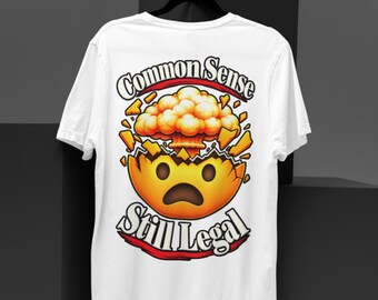 May include: A white short-sleeve t-shirt featuring a graphic on the back. The design shows a yellow emoji head cracking open with an orange mushroom cloud explosion emerging from the top. The text reads Common Sense Still Legal in black.