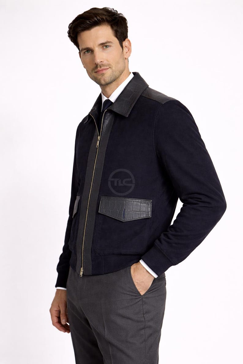 May include: A navy blue jacket with leather detailing on the shoulders, pockets, and zip. The jacket has a full-length zip and a logo on the chest. Worn with a white shirt and grey trousers.