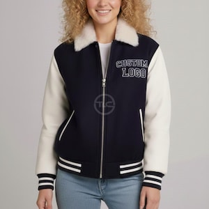May include: Navy blue and cream varsity jacket with a faux fur collar. The jacket features white sleeves, a zipper closure, and the text "CUSTOM LOGO" on the chest. The cuffs and hem have white stripes.