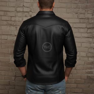 Puede incluir: Camisa de cuero negra con cuello cl&aacute;sico y mangas largas. La camisa presenta un detalle de canes&uacute; en la espalda y un logotipo sutil. Las mangas est&aacute;n dobladas. El modelo lleva vaqueros azules.