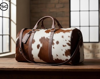 May include: A brown and white cowhide duffel bag with brown leather handles, straps, and a luggage tag. The bag is on a wooden surface, with a window and brick wall in the background.
