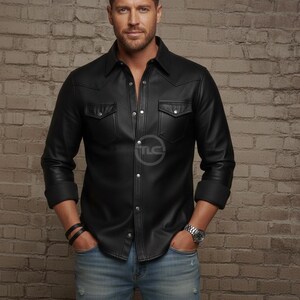 Puede incluir: Una camisa de cuero negro con dos bolsillos en el pecho y botones plateados. La camisa se lleva con vaqueros azul claro y un reloj plateado. El modelo est&aacute; de pie frente a una pared de ladrillos.