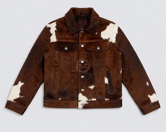 May include: A brown and white cowhide jacket with a classic collar, two chest pockets, and silver buttons. The jacket has a Western-inspired design with a natural fur texture and a button-up front. A stylish outerwear piece.